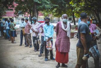 The needy people line up with social distancing for their share of hot meals.